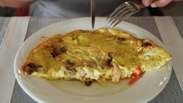 Closeup view 4k video of white plate and big fresh hot egg omelette stuffed with mushrooms, sweet red pepper, sausages and cheese. Woman eats healthy breakfast.