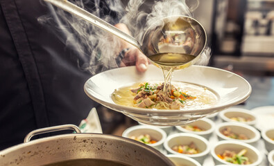 Chef pours broth into a chicken soup with noodles, meat and vegetable