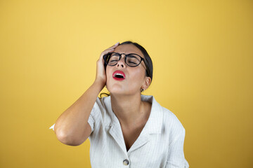 Beautiful woman over yellow background putting one hand on her head smiling like she had forgotten...