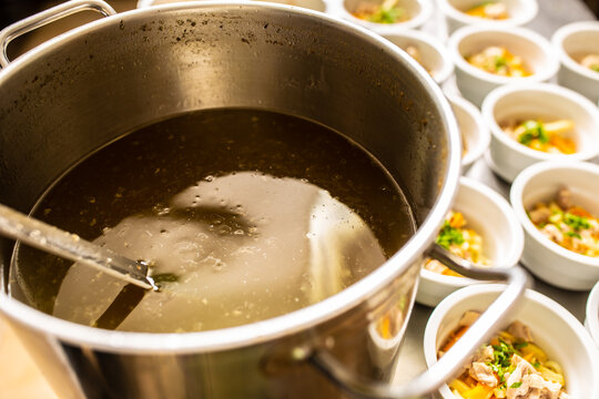 Pot of broth next to lined up bowl of chicken soup