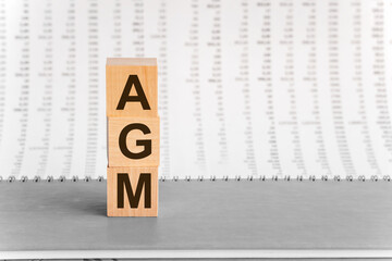 AGM - Annual general meeting - acronym on wooden cubes on columns of numbers background. Business...