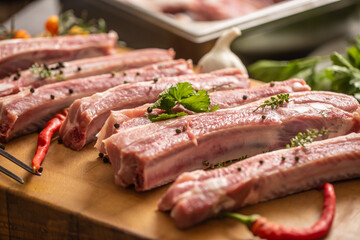 Raw seasoned spare ribs on a cutting board with chillies next to it