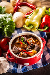 Bowl of goulash soup with meat, potatoes and chillies next to raw ingredients for the stew