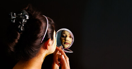 an indian lady with face pack applied in half dried condition checking her face in a mirror with selective focus on the mirror image