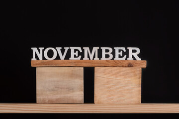 Word November by wooden letters on black background. Front view. Autumn calendar. Fall month