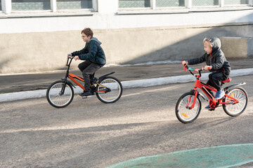Fototapeta premium Two children ride bicycles on the paved road. Biking with friend