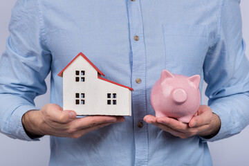 Man holding model house and piggy Bank. Savings for buying home. Economical buy housing