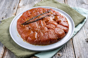 Traditional French tarte tatin with apples and vanilla offered as close-up on a modern Nordic design plate with rustic background