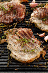 Grilled pork neck with herbs and garlic on a cast iron grill plate, top view