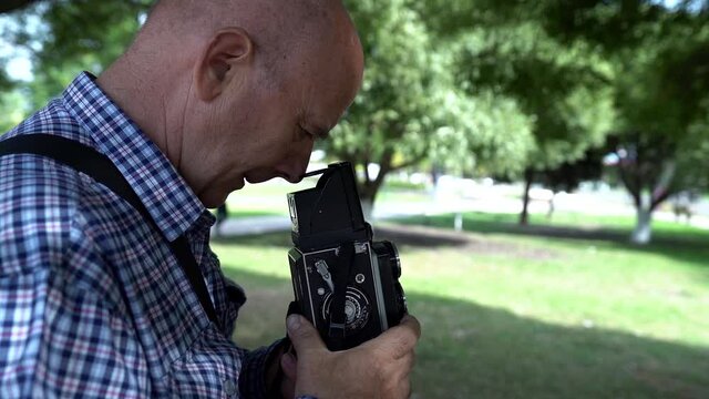 Grandpa is holding an unusual camera. An elderly man in a shirt on the street. The concept of a photographer in nature in a Park with a background of trees.