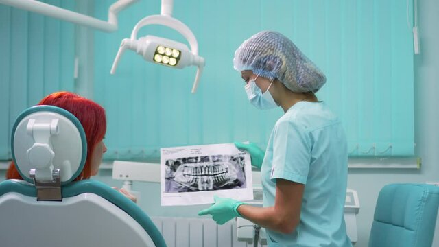 A young woman dentist shows a panoramic x-ray of the jaw to a patient in a dental clinic. Medium shot.