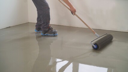 A worker rolls out the liquid floor with a trowel. Squeegee for distributing the mixture. The...