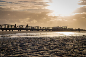 Fototapeta premium People on wooden seabridge at north sea beach in Sankt Peter-Ording, Germany.