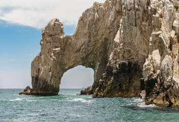 Fototapeta na wymiar Cabo San Lucas, Mexico - April 22, 2008: South end of Baha California. Closeup of the Arch in beige rocks formation. Greenish ocean water in front under blue cloudscape.