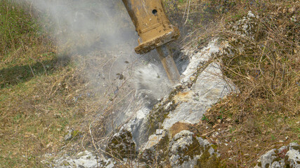 CLOSE UP: Dust rises as breaker attachment demolishes rocks during roadworks.