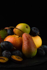 Still life of pears, apples and plums on a black background.
