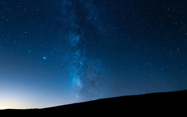 Milky way up a hill in a starry night sky. Blue sky with stars without light pollution.