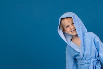 A child in a bathrobe playfully peeks out from the right against a blue background. Studio shot with space for text for pool, spa, sauna and bath wash.