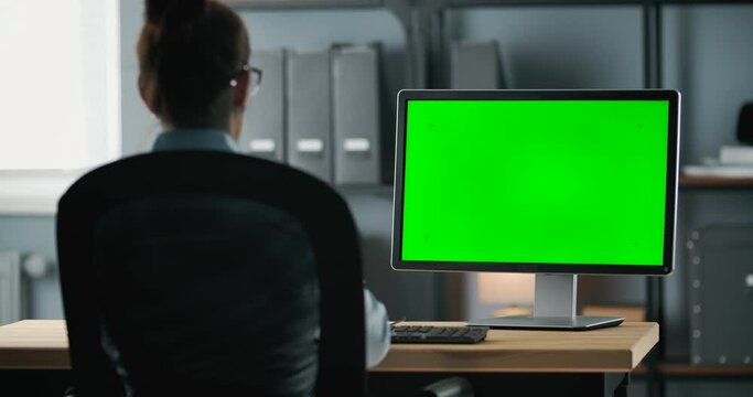 Businesswoman in formal clothing sitting at bright modern office and working on computer with empty green screen. Successful female using personal laptop at workplace.