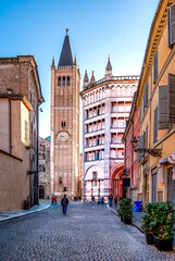The bell tower of Parma Cathedral and the baptistery seen from Strada Duomo, in Parma historical center, Emilia Romagna region, Italy. Sunny day with bright sky and few people walking.