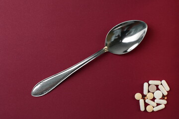 Pills and tablets and a spoon are depicted on a burgundy background