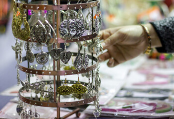 Hand of a lady selecting ear rings metal junk jewellery at a shop.