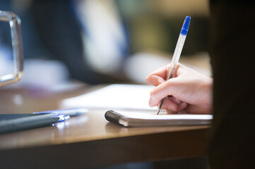 Fototapeta premium Woman Writes With Pen On A Note Book At A Meeting