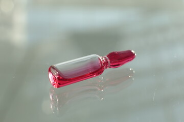 A glass vial with a red solution lies on a glass table
