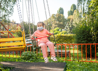 A little girl in a protective mask rides a carousel during the coronavirus epidemic.

