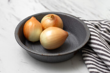 Sweet Yellow Onions Known as Candy Onions in a Gray Bowl on a White Countertop, Gray and White Striped Dish Towel beside Bowl
