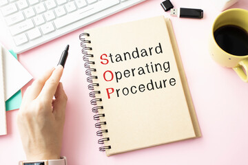 Standard Operating Procedure text on paper in open diary with spectacles, colourful push pin, pen and calculator on the wooden table - business and finance concept