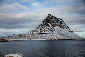 View of the mountain Kirkjufell in the Snæfellsnes peninsula in Iceland surrounded by ocean water and clouds
