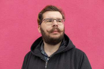 hipster person with beard and mustache middle adult age posing portrait photography looking side ways on pink wall textured background