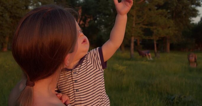 Happy mother holds her toddler, they look around and have a talk and joy at park