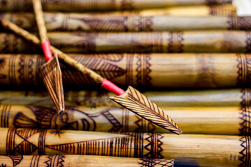 arrow showing hand made wooden bamboo carving engraved fish figure artwork on bamboo, rows of engraved bamboo sticks. tribal artwork. textured background