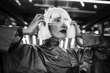 A woman in a futuristic metallic dress with glasses looks ahead.