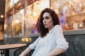 Young woman sitting at a table on the street in the evening.