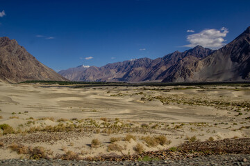 arid lands of ladakh with barren himalayan peaks viewable in distance with deep blue sky.