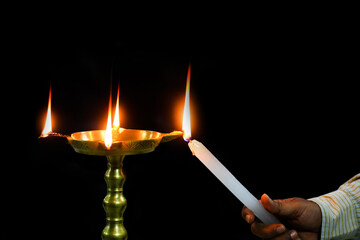 oil brass lamp diya being lit by a candle for inauguration ceremony holy worship in isolated dark black background