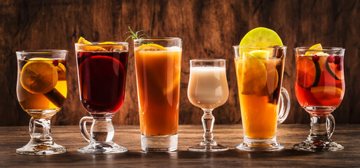 Selection of autumn or winter alcoholic hot drinks and cocktails - mulled wine, glogg, grog, eggnog, warm ginger ale, hot buttered rum, punch, mulled apple cider on wood background, copy space