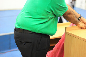 side view of a large tummy of a morbid obese person without face in green t-shirt and black trousers