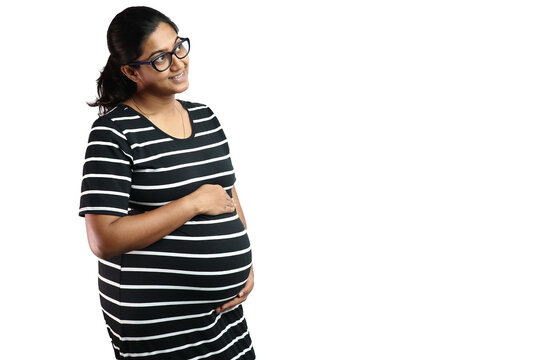 A pregnant lady wearing spectacles with black dress with white stripes and hands on belly looking up in delight with copy space for text