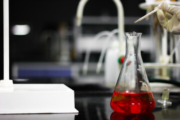 pouring a red chemical on a glass conical flask with a dropper in a chemistry lab