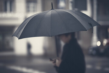 Silhouette with umbrella in rainy foggy day. Focus on umbrella, man in bokeh. Person with umbrella stands by road in rainy weather. Black umbrella, soft selective focus.