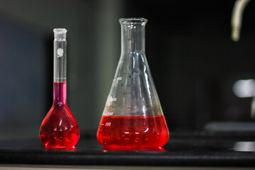 red liquid in a conical flask and round bottomed flask on a black granite table in dark background