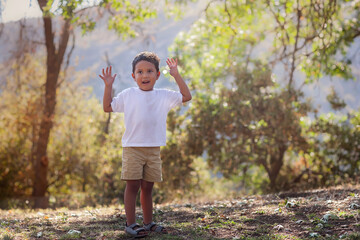Young boy advancing to preschool age is outdoors learning to catch a ball with  his arms up in th air, in southern California setting.