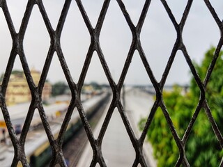 view of a blurred sky railway station through diamond shaped grill