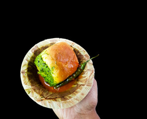 Vada pau bread and green sauce on a plate in dark background on hand