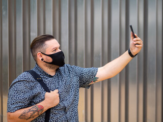 Hombre de negocios joven y tatuado andando por la calle usando su teléfono movil vistiendo...