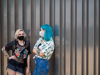 Mujeres jóvenes con mascarilla hablando respetando las medidas de seguridad y distanciamiento...